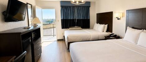 Une chambre d’hôtel avec deux lits, un bureau avec une télévision, un balcon avec vue et un lustre moderne.