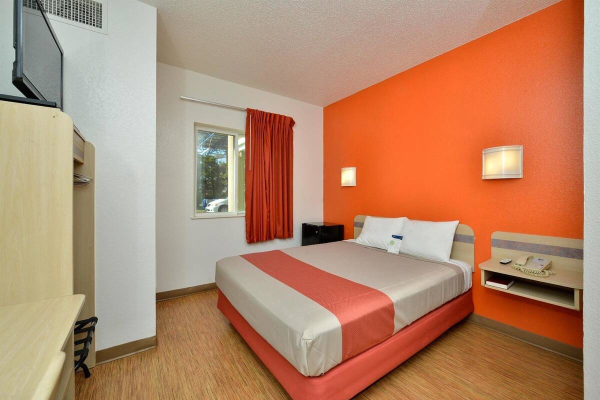 Una habitación de hotel con cama, mesita de noche, armario y ventana con cortinas.