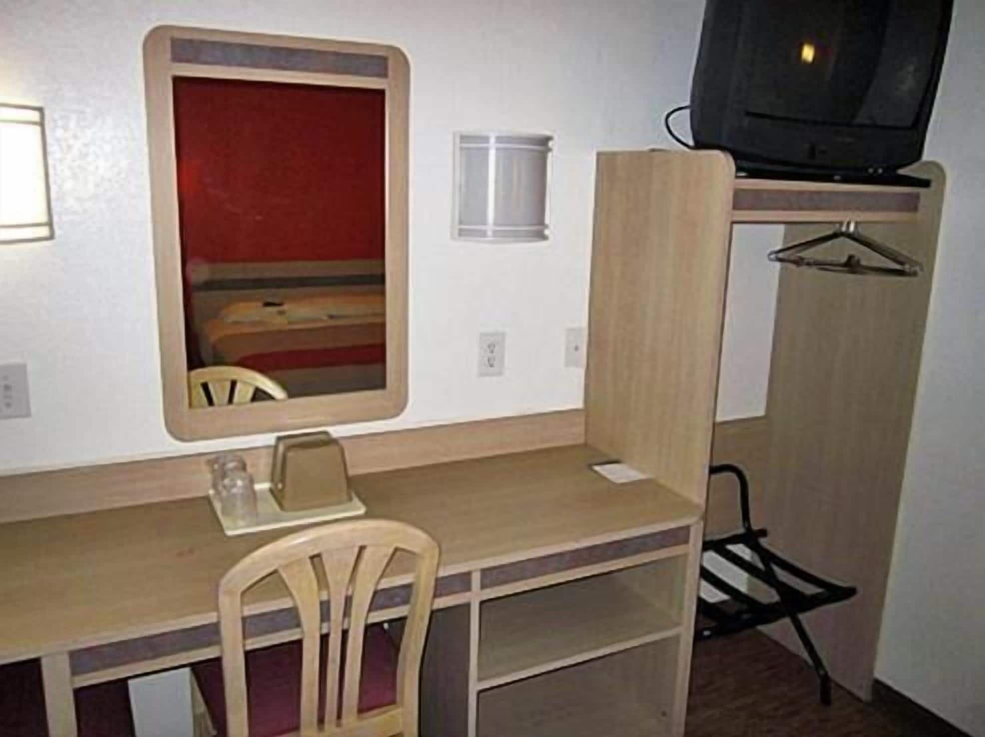 A compact room with a wooden desk, a chair, a mirror, a television, and a small window.