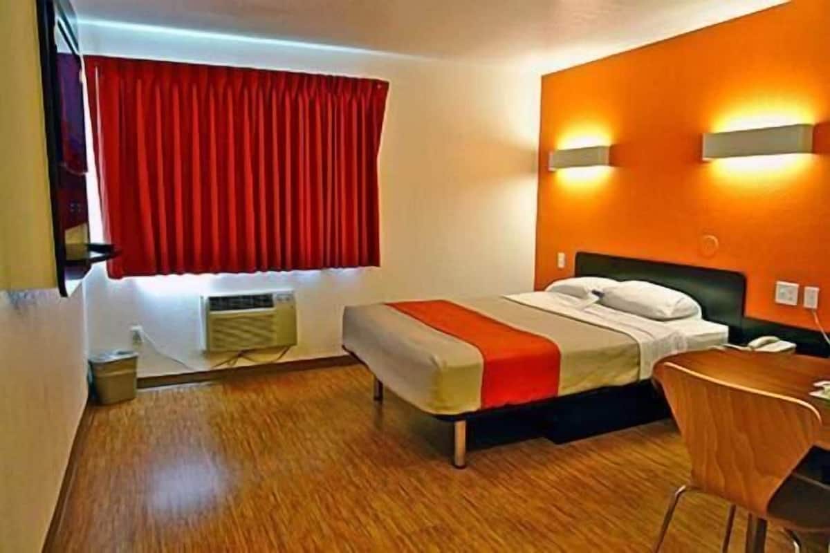 Una habitación de hotel con cama, escritorio y ventana con cortinas rojas.
