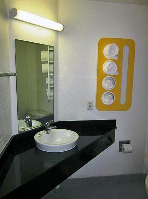 A bathroom with a white sink, black countertop, and a mirror. There is a yellow towel dispenser with four towels.