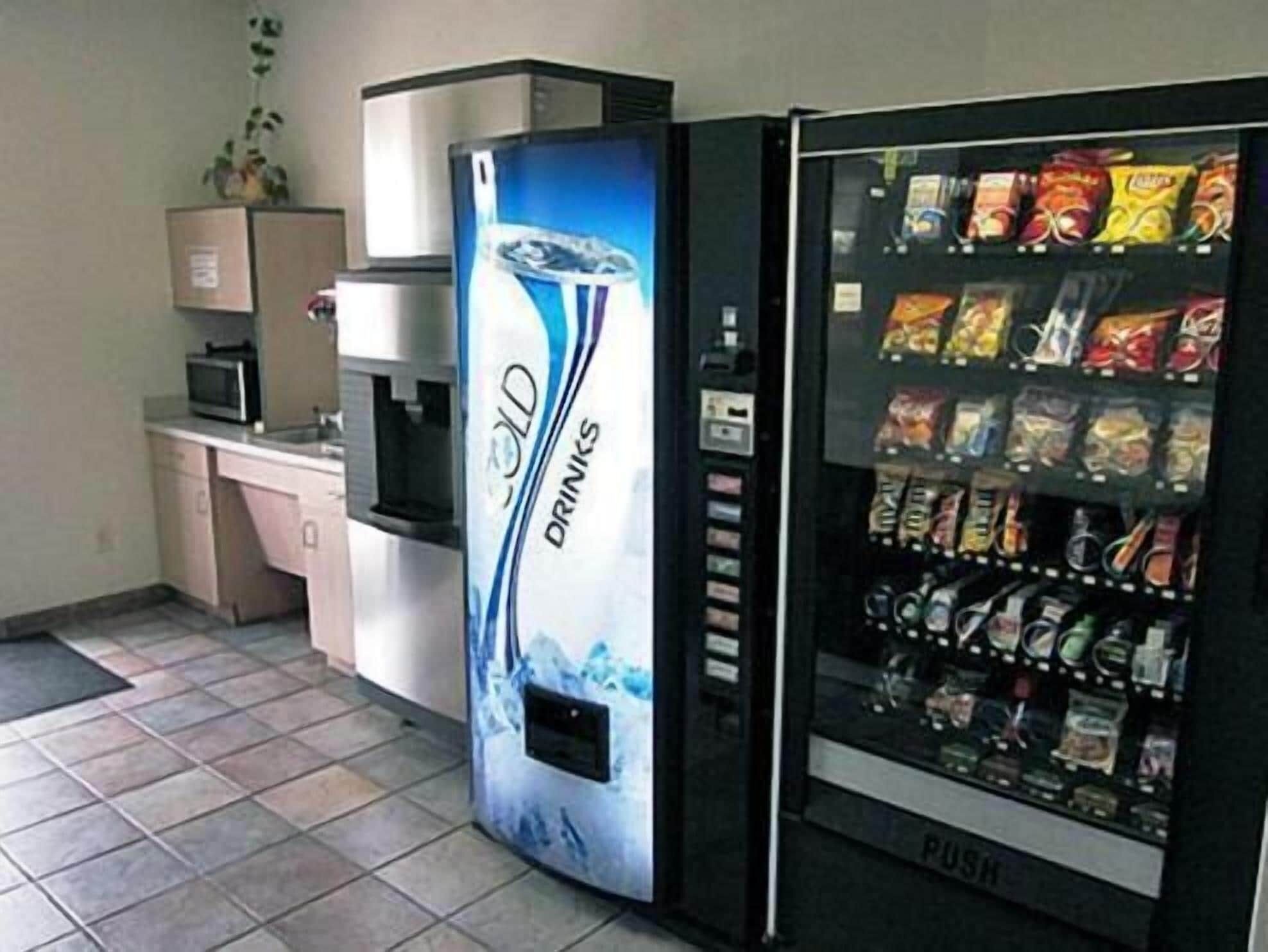 A vending machine with a drink dispenser and a snack vending machine in a room with tiled flooring and a microwave on a counter.
