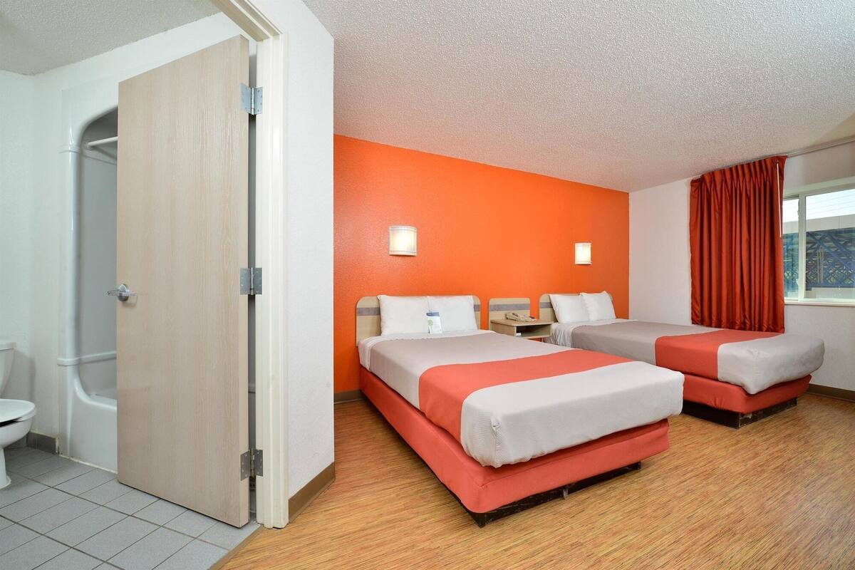 Una habitación de hotel con dos camas, baño y ventana con cortinas.