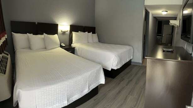 A hotel room with two beds, a desk, a mirror, and a wall-mounted light. - Americas Best Value Inn & Suites Groves Port Arthur (Groves)
