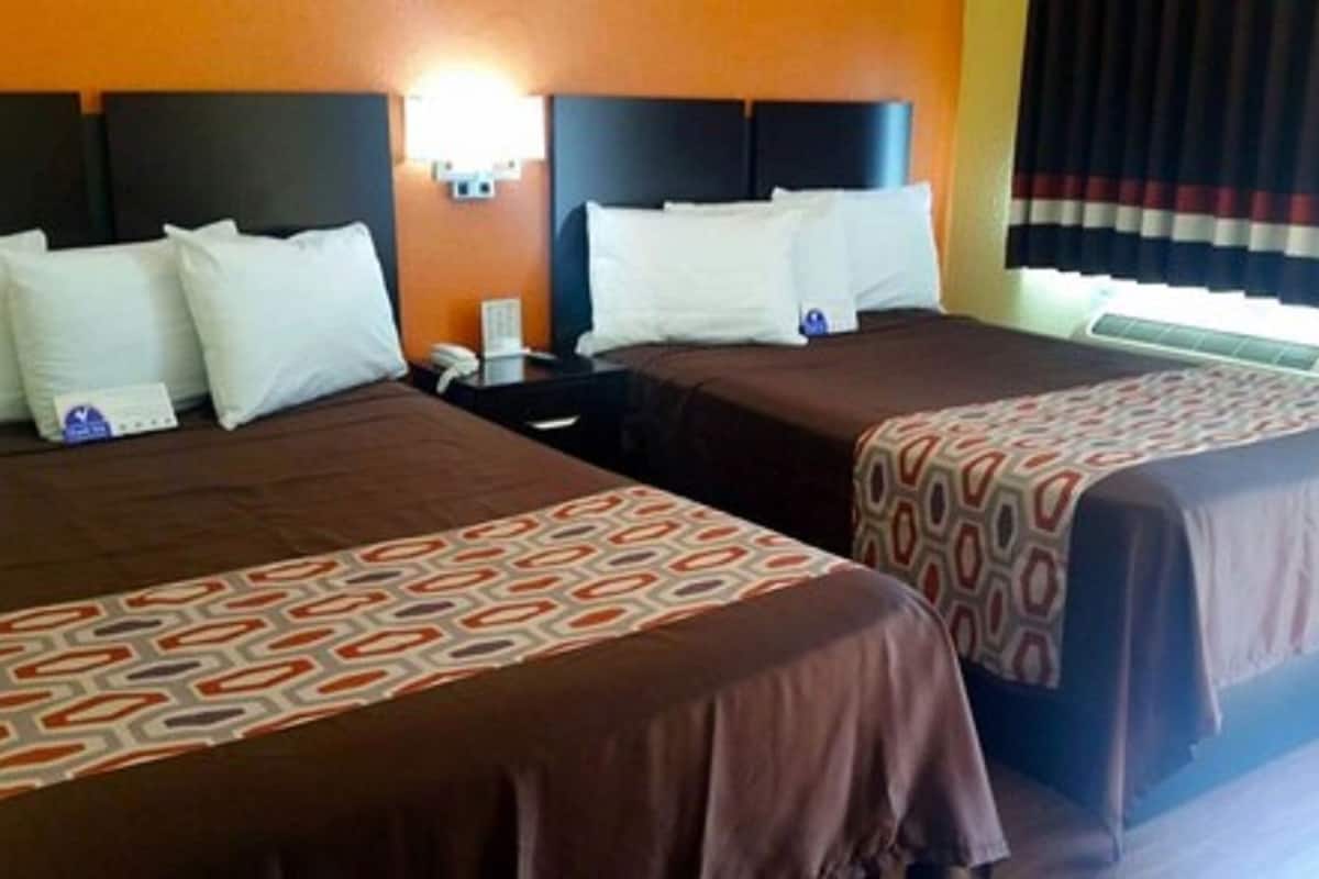 Ein Hotelzimmer mit zwei Betten, jeweils mit einer gemusterten Tagesdecke, einem Nachttisch, einem Telefon und einer wandmontierten Lampe.