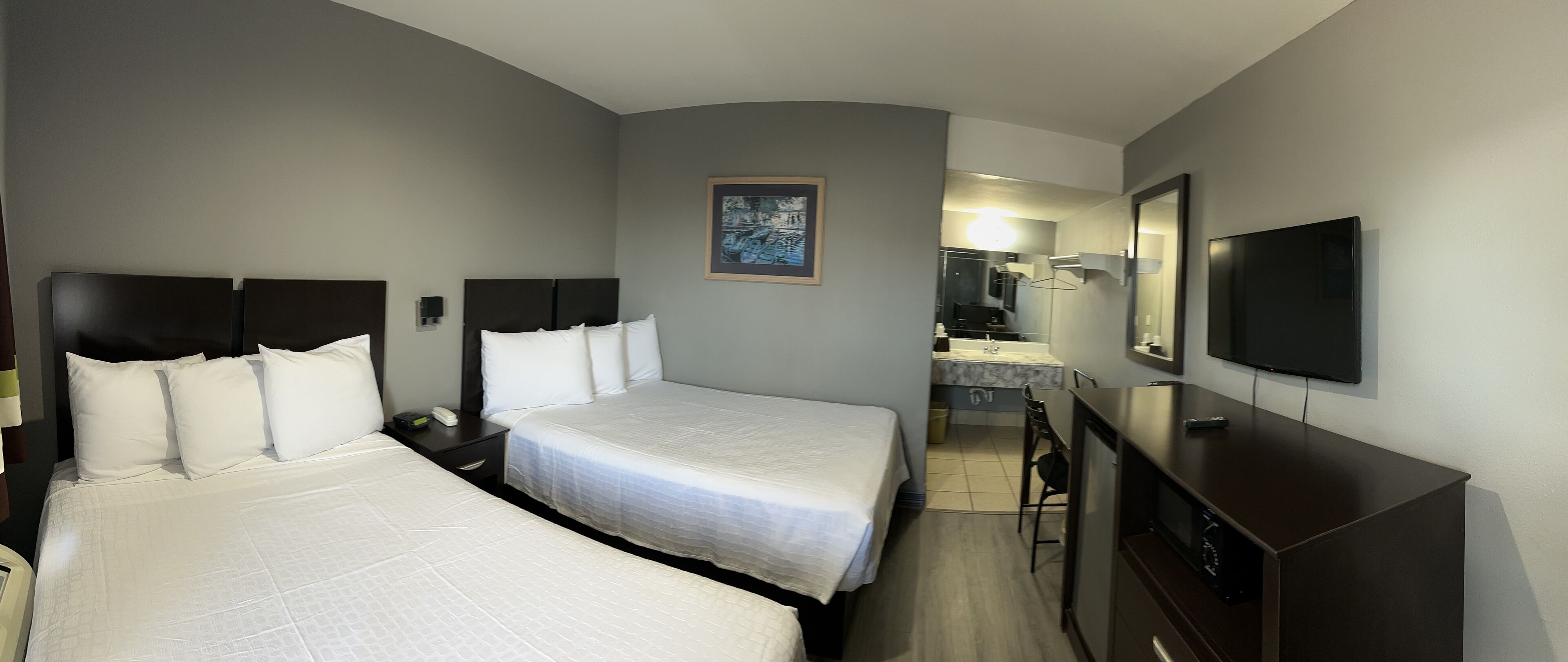 A hotel room with two beds, a TV, a desk, and a bathroom visible in the background.