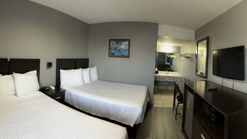 A hotel room with two beds, a TV, a desk, and a bathroom visible in the background.