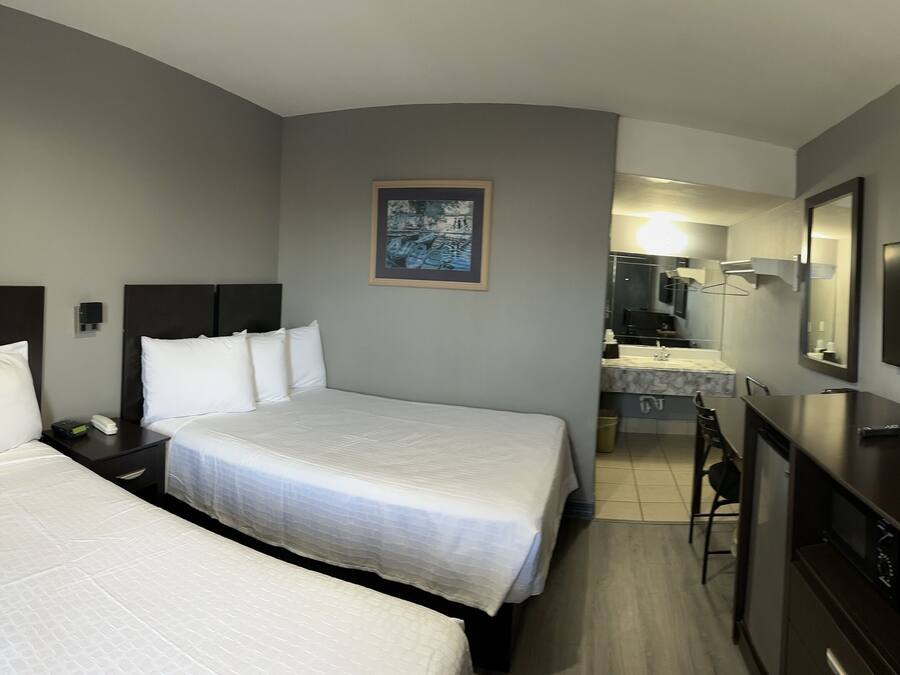 A hotel room with two beds, a TV, a desk, and a bathroom visible in the background.