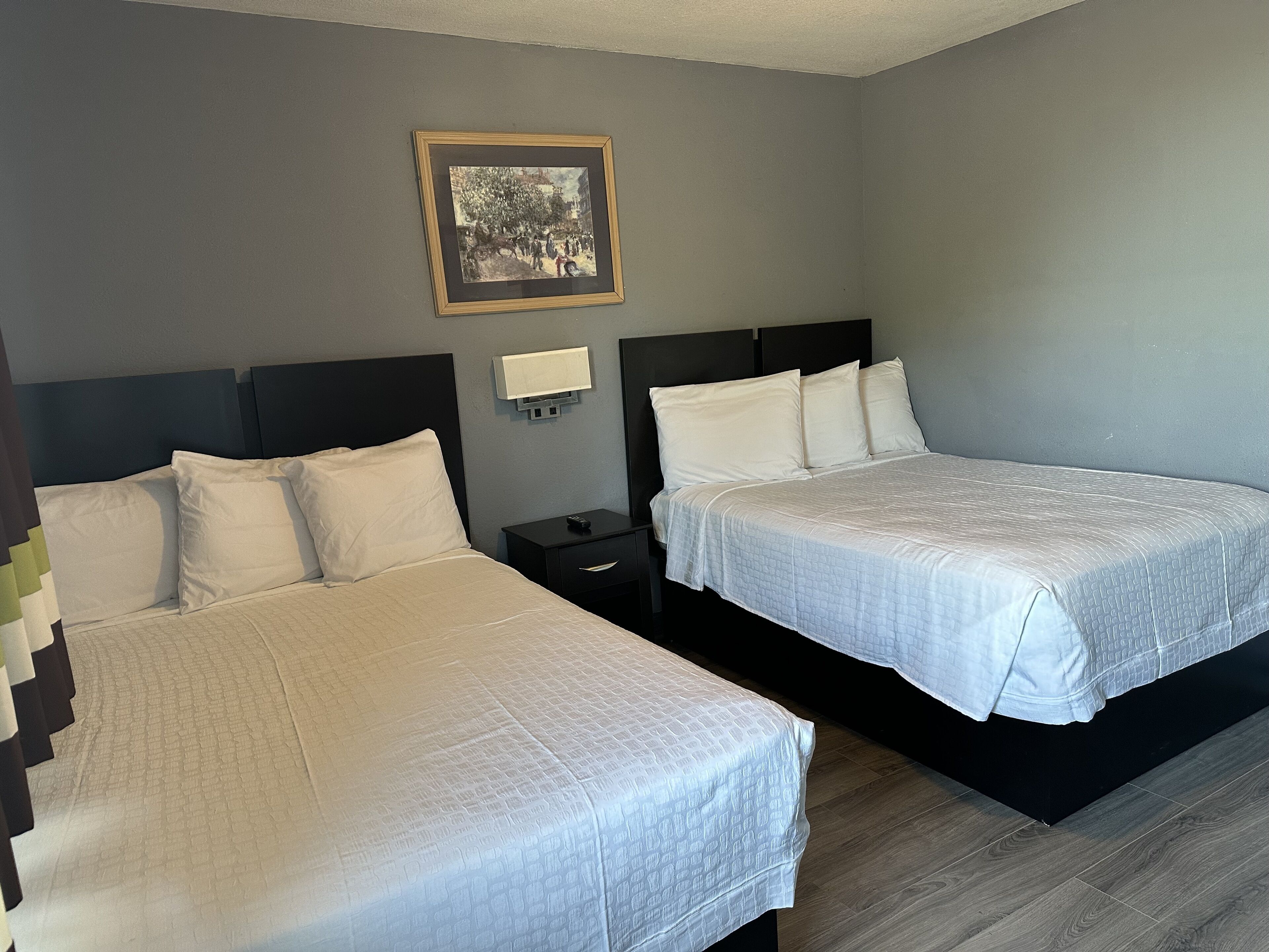 Une chambre d’hôtel avec deux lits, une table de chevet, un tableau encadré au mur et une lampe fixée au mur.