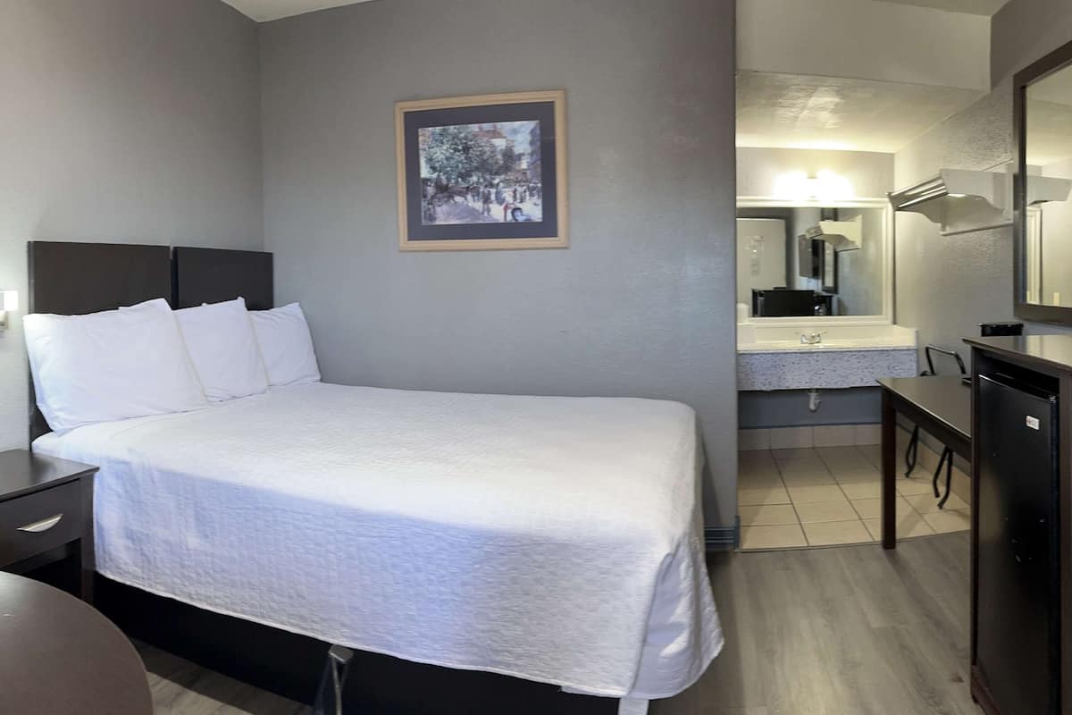 Ein Hotelzimmer mit Bett, Nachttisch, Kommode, Spiegel und einem Badezimmer mit Waschbecken und Spiegel.