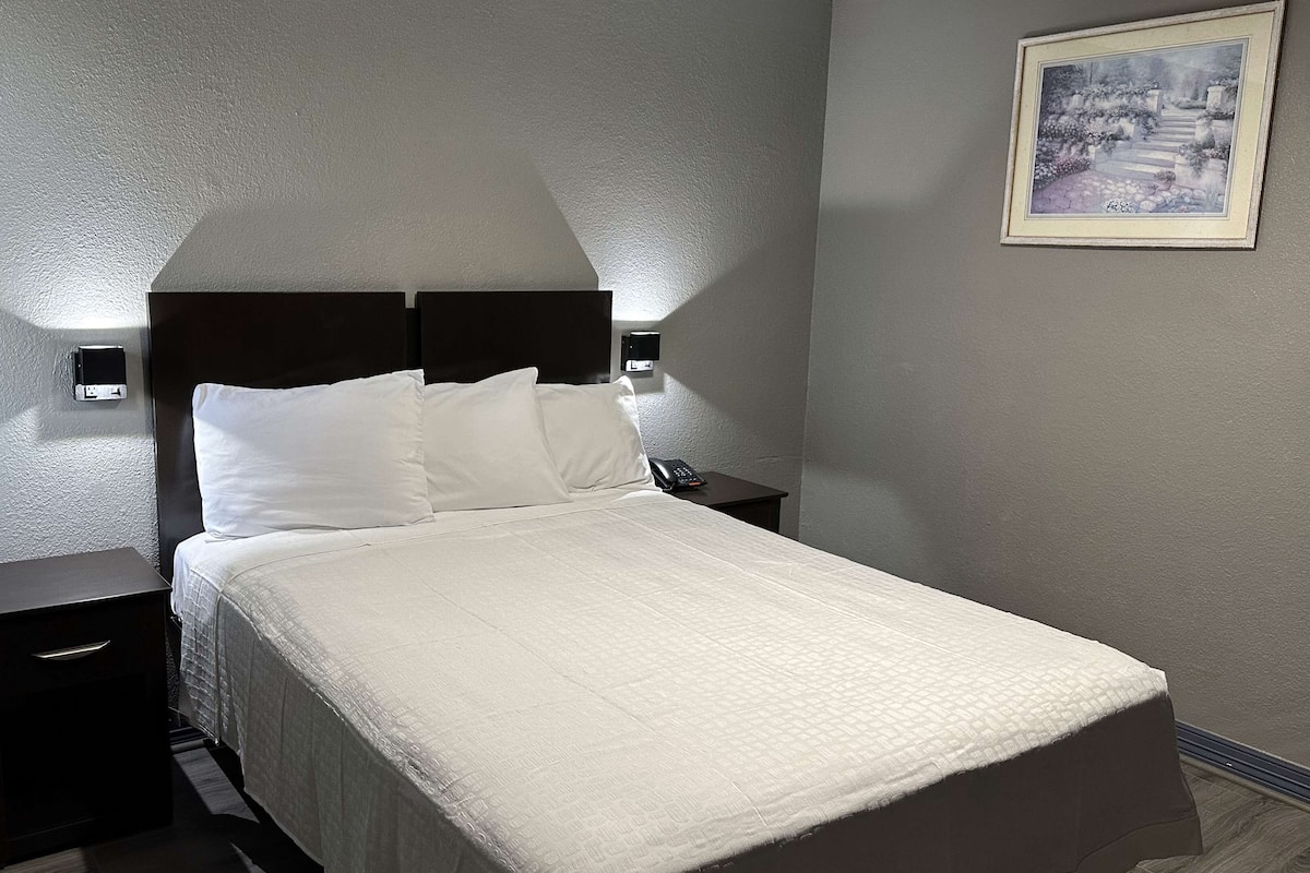 Ein ordentlich bezogenes Bett mit weißen Leinen, zwei Nachttische mit schwarzer Furnierung und ein gerahmtes Bild an der Wand.