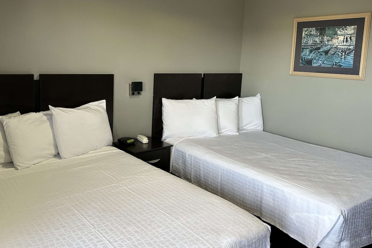 Ein Hotelzimmer mit zwei Betten, einem Nachttisch, einem Telefon und einem Gemälde an der Wand.