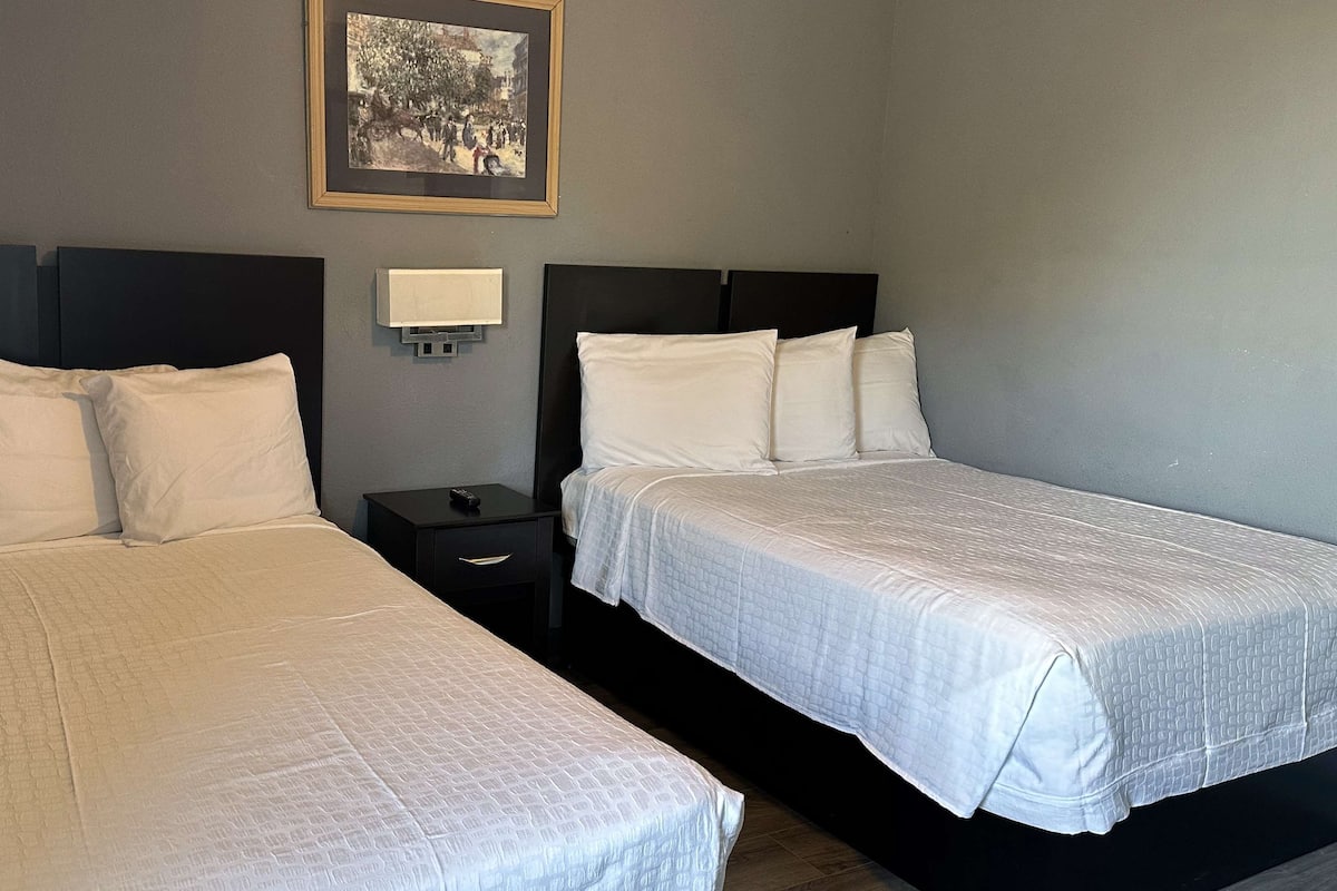 Ein Hotelzimmer mit zwei Betten, einem Nachttisch, einer Wandleuchte und einem gerahmten Bild.