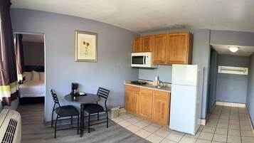 A compact hotel room with a kitchenette, a bed, a dining area with two chairs, and a framed picture on the wall.