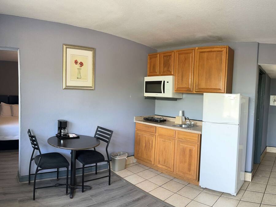 A compact hotel room with a kitchenette, a bed, a dining area with two chairs, and a framed picture on the wall.