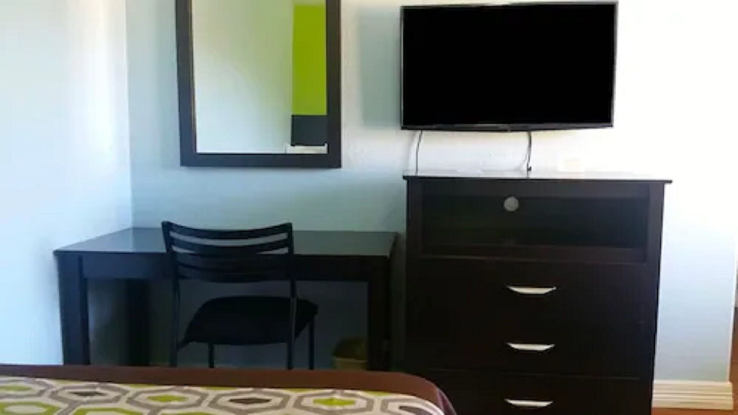 Une chambre comprenant un lit, un bureau, une chaise, une commode et un téléviseur fixé au mur.