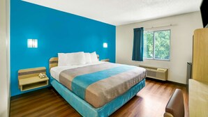 A hotel room with a large bed, a bedside table, a window with curtains, and a wall-mounted heater. - Motel 6 Gordonville PA - Lancaster PA (Gordonville)