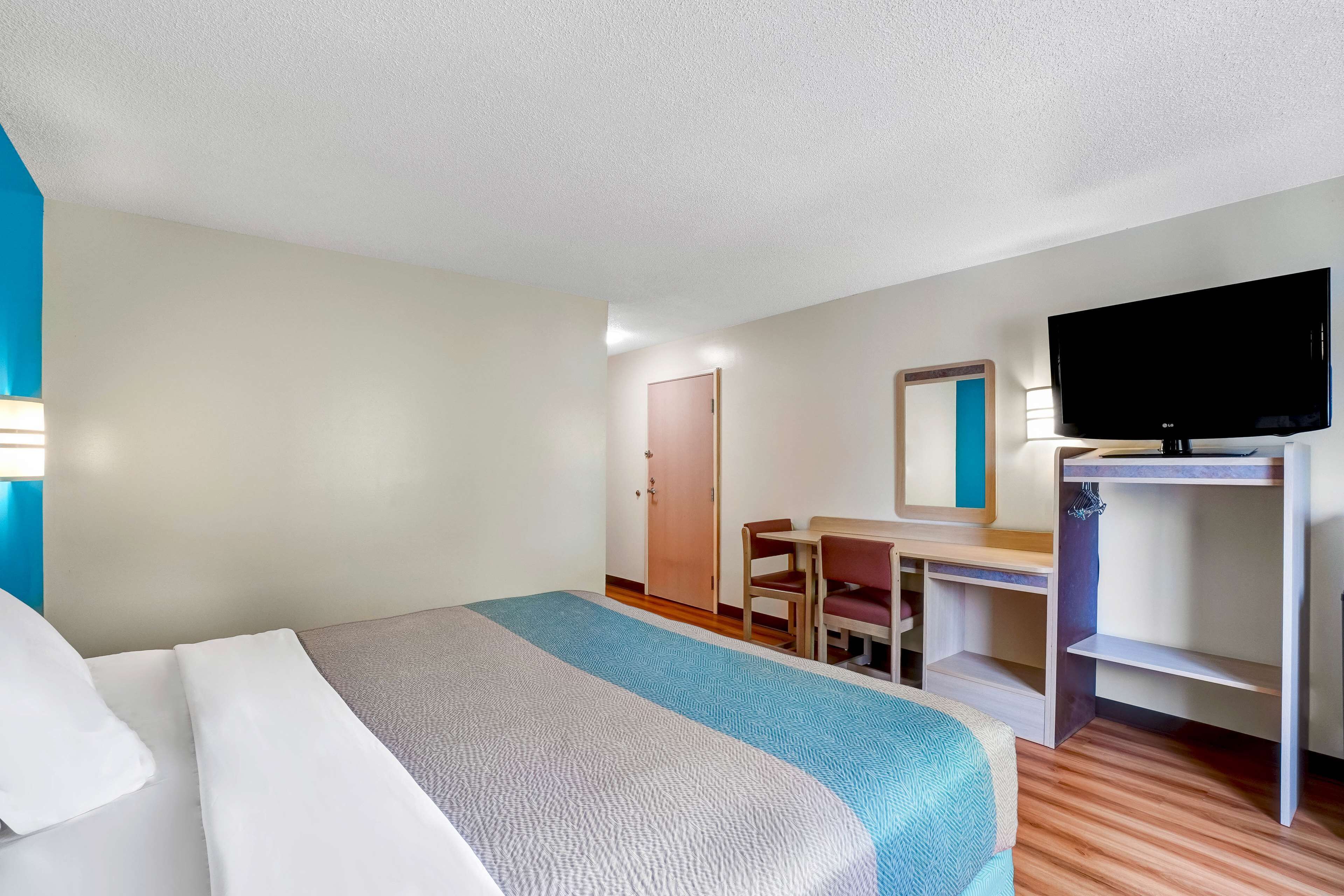 A hotel room with a bed, a desk, a chair, a television, and a door.