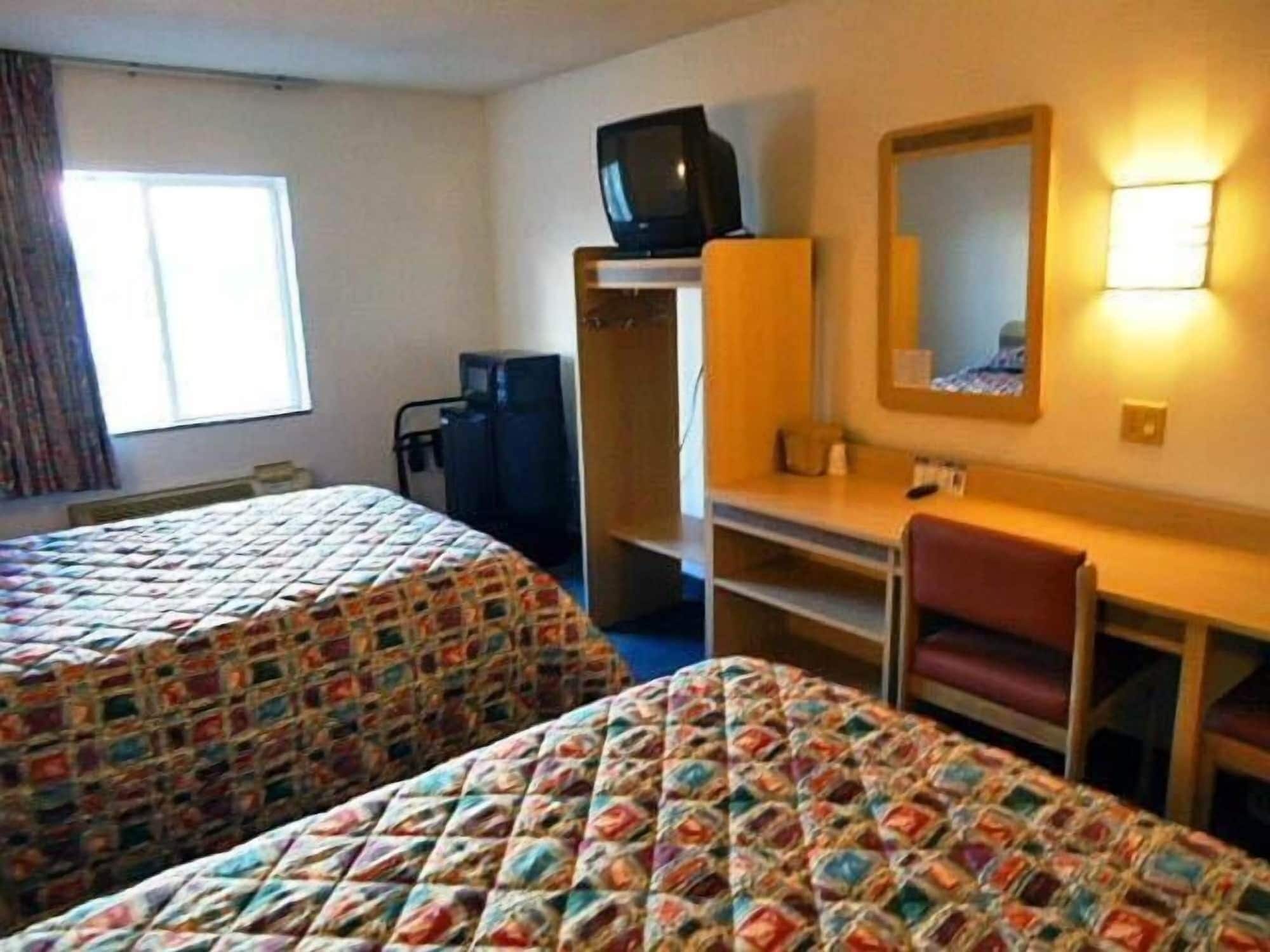 A hotel room with two beds, a desk, a chair, a television, and a mirror.