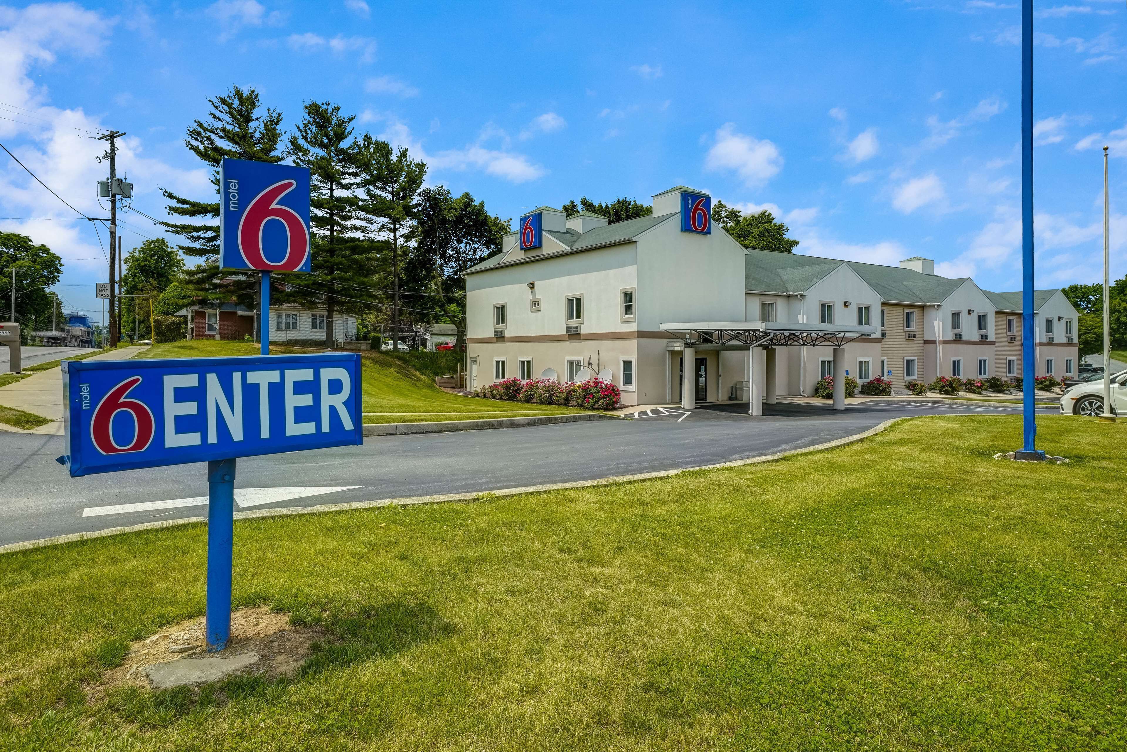 Un motel con un cartel que dice '6 ENTER', una zona de estacionamiento techada y un edificio con múltiples ventanas y techo verde.