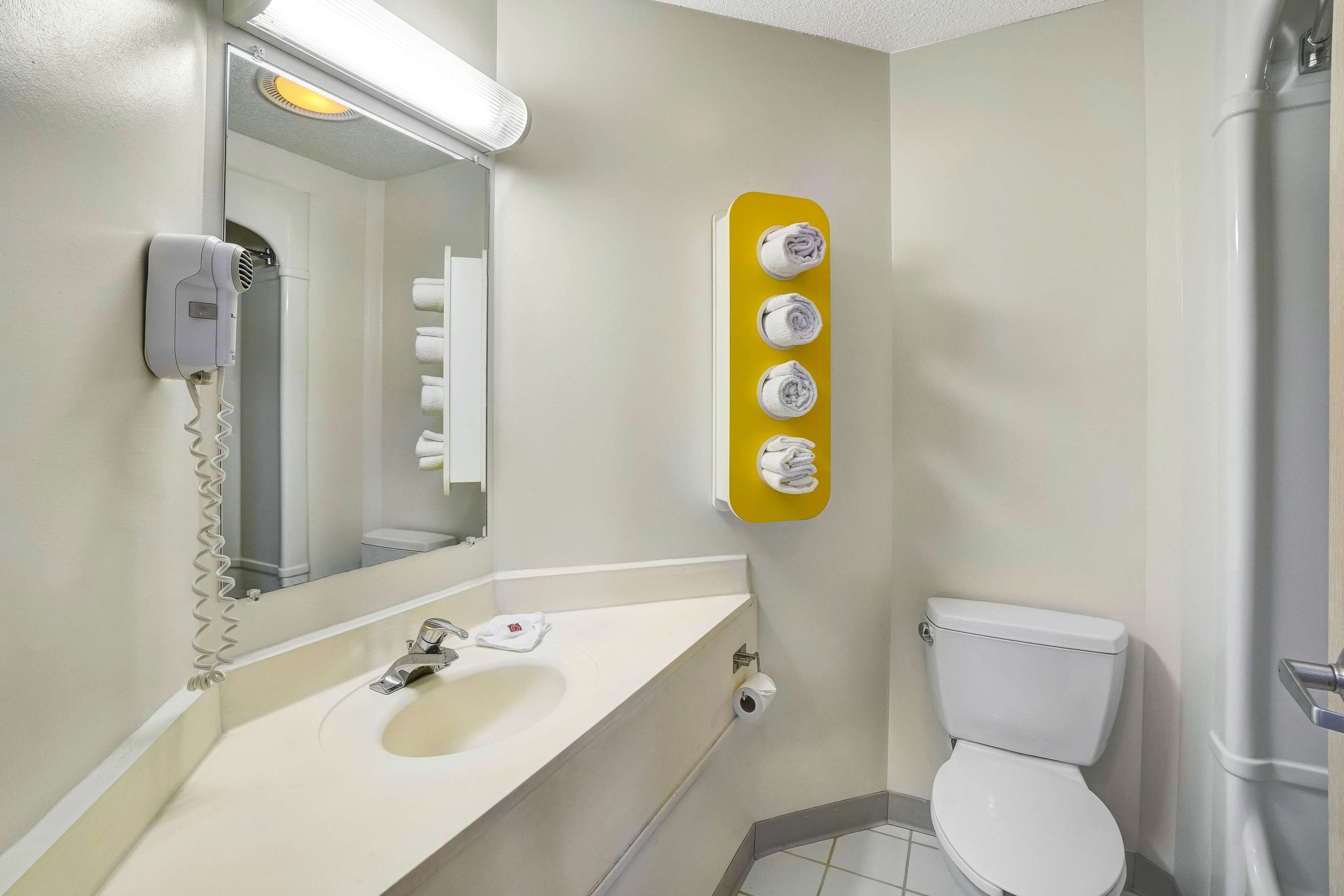 A bathroom with a sink, mirror, hair dryer, toilet, and a towel rack.