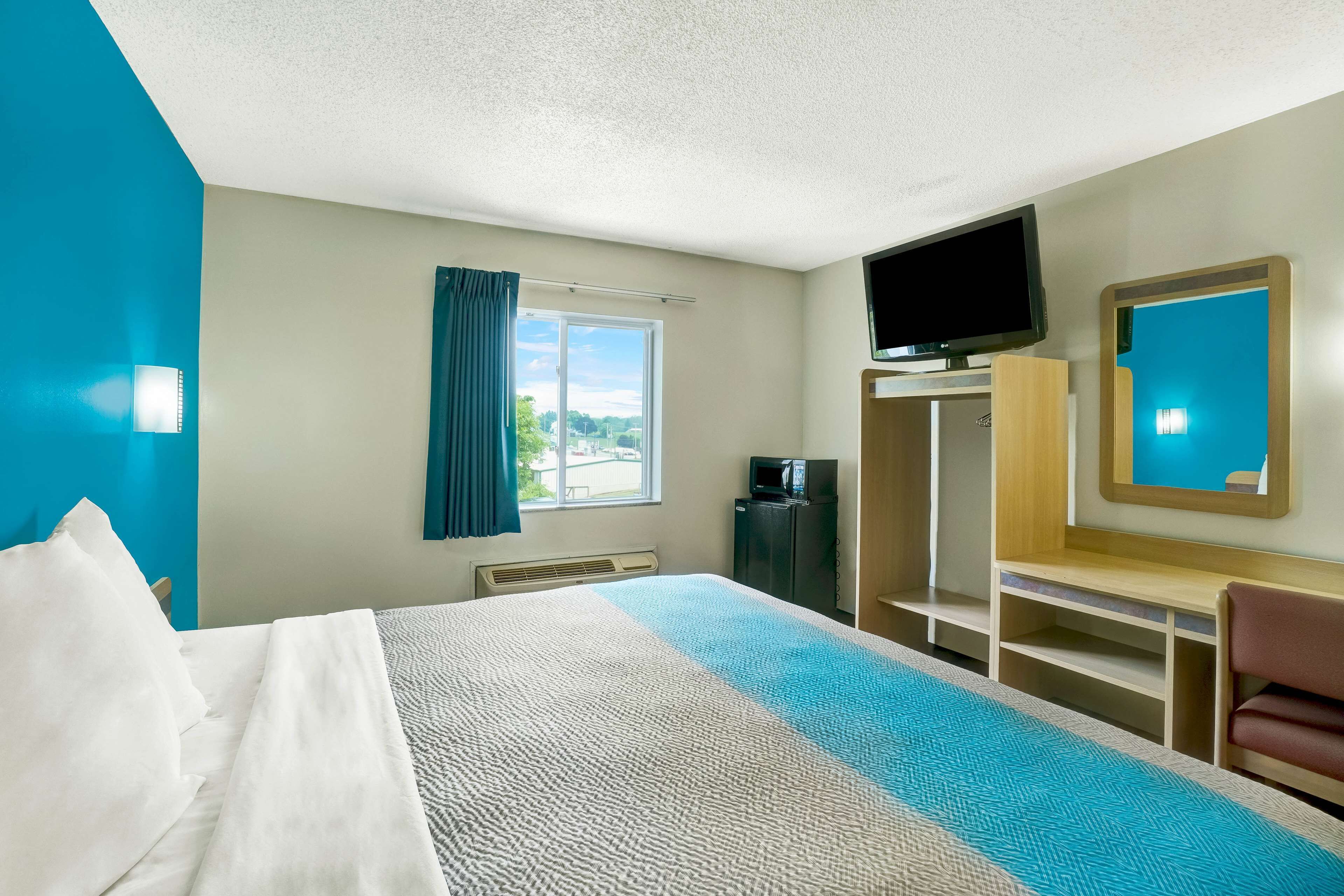 A hotel room with a bed, a desk, a TV, and a view of the outdoors.
