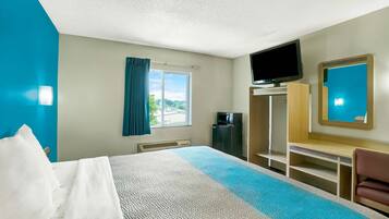 A hotel room with a bed, a desk, a TV, and a view of the outdoors.