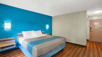 Une chambre d’hôtel avec un lit, une table de chevet, une étagère fixée au mur et une porte.
