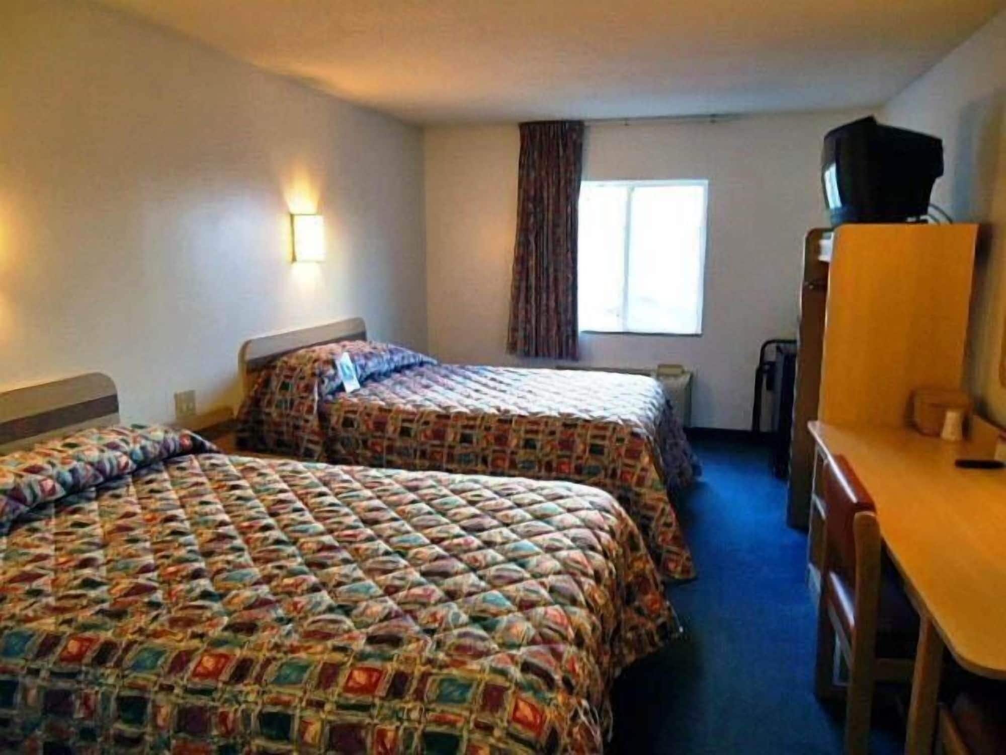 Habitación de hotel con dos camas, un escritorio, una silla, un televisor y una ventana con cortinas.