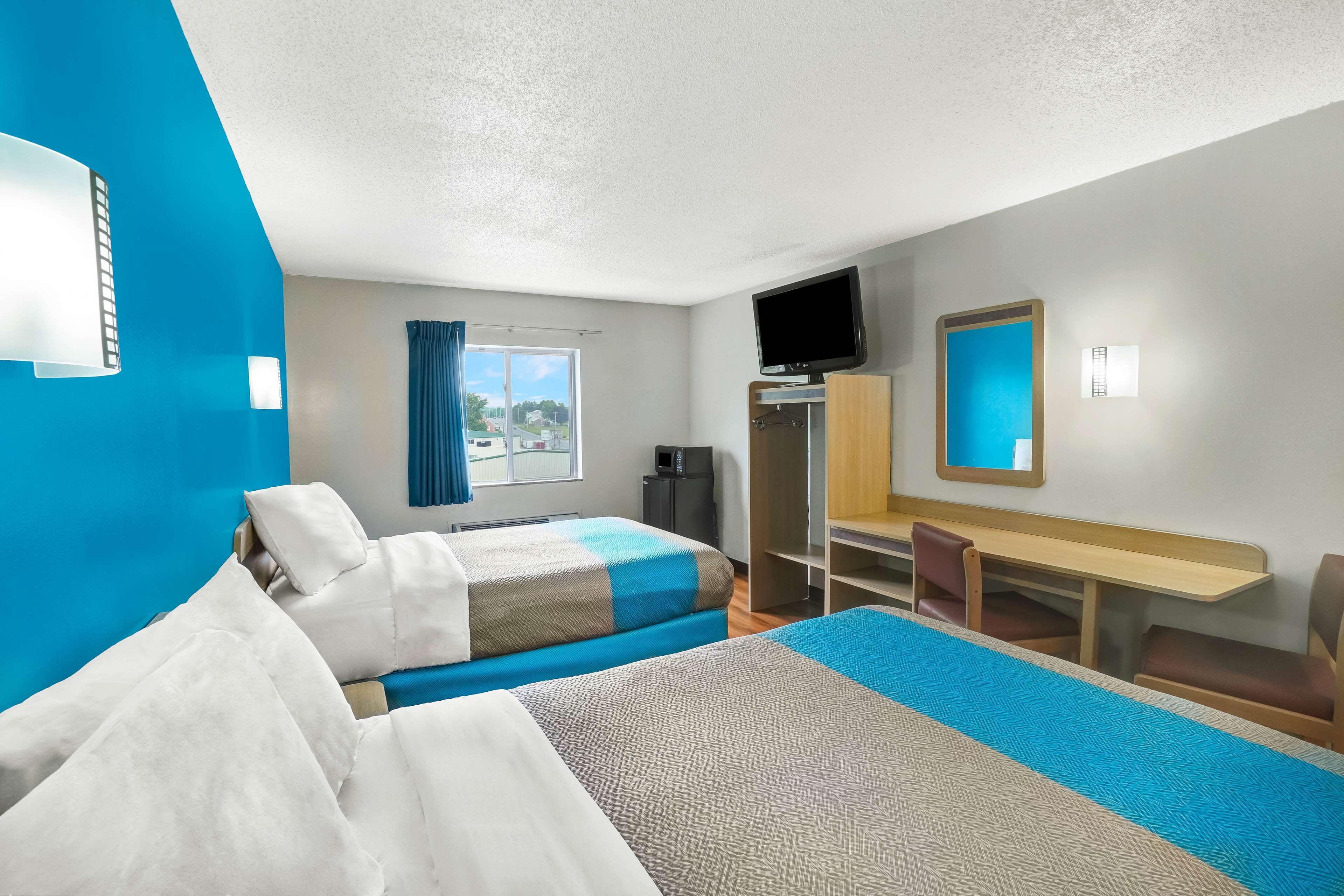 A hotel room with two beds, a desk, a TV, and a window with curtains.
