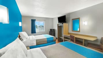 A hotel room with two beds, a desk, a TV, and a window with curtains.
