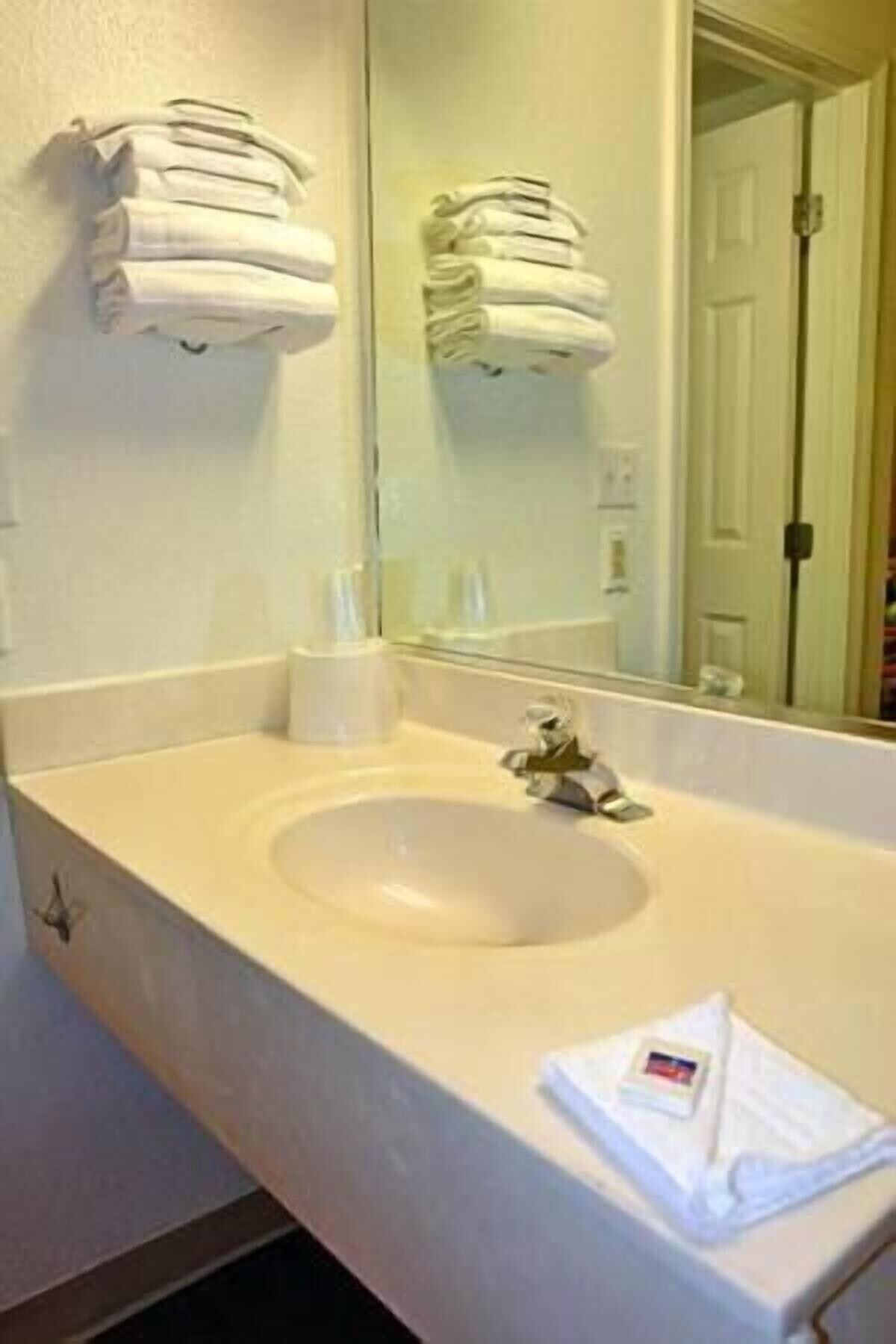 A bathroom with a sink, mirror, and towels stacked on the wall.