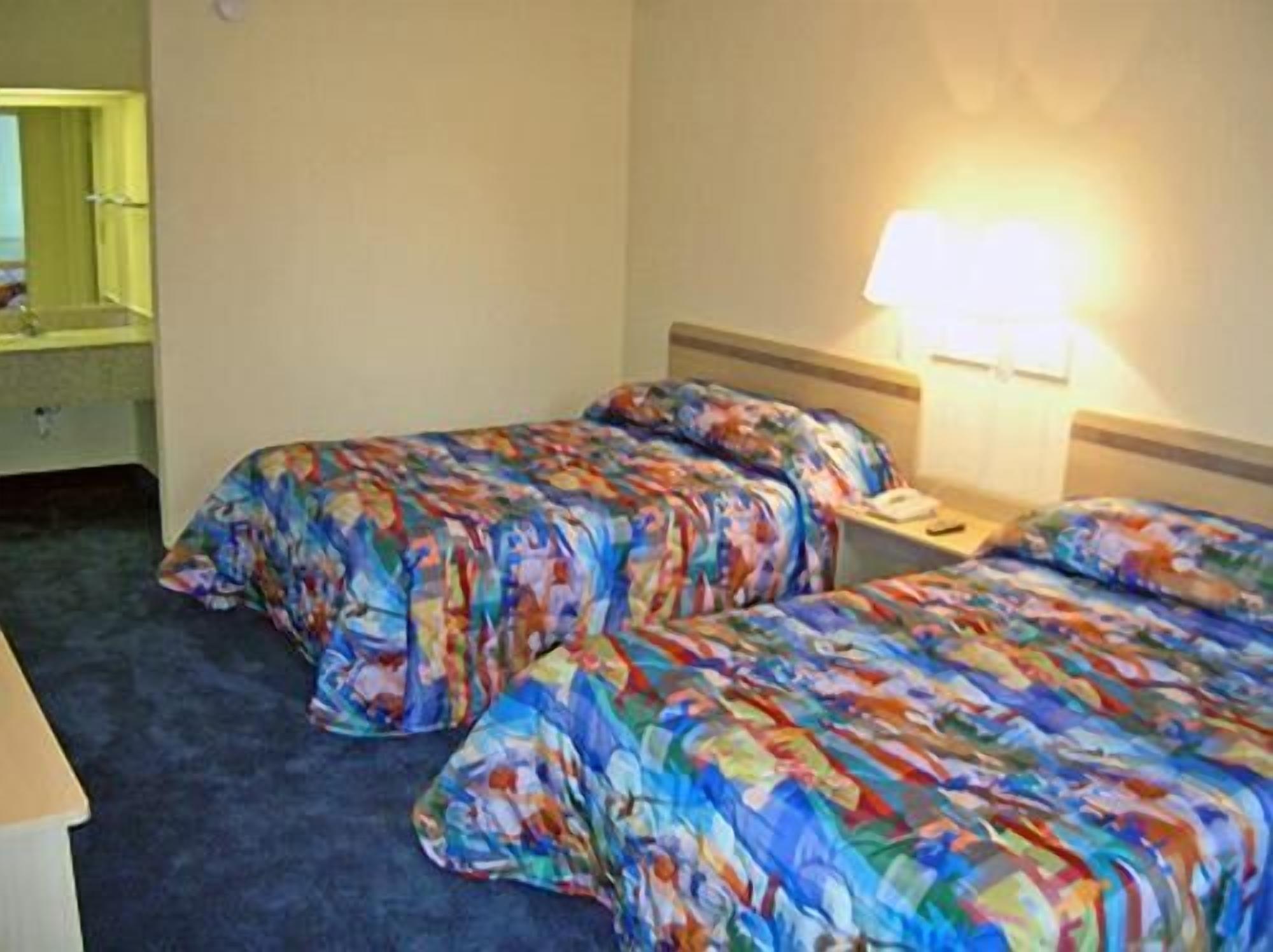 A hotel room with two beds, a bedside table, a lamp, and a mirror.
