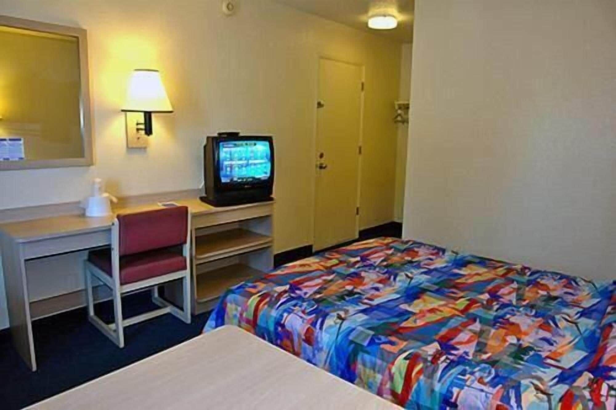 Una habitación de hotel con cama, escritorio con silla, televisor y armario.