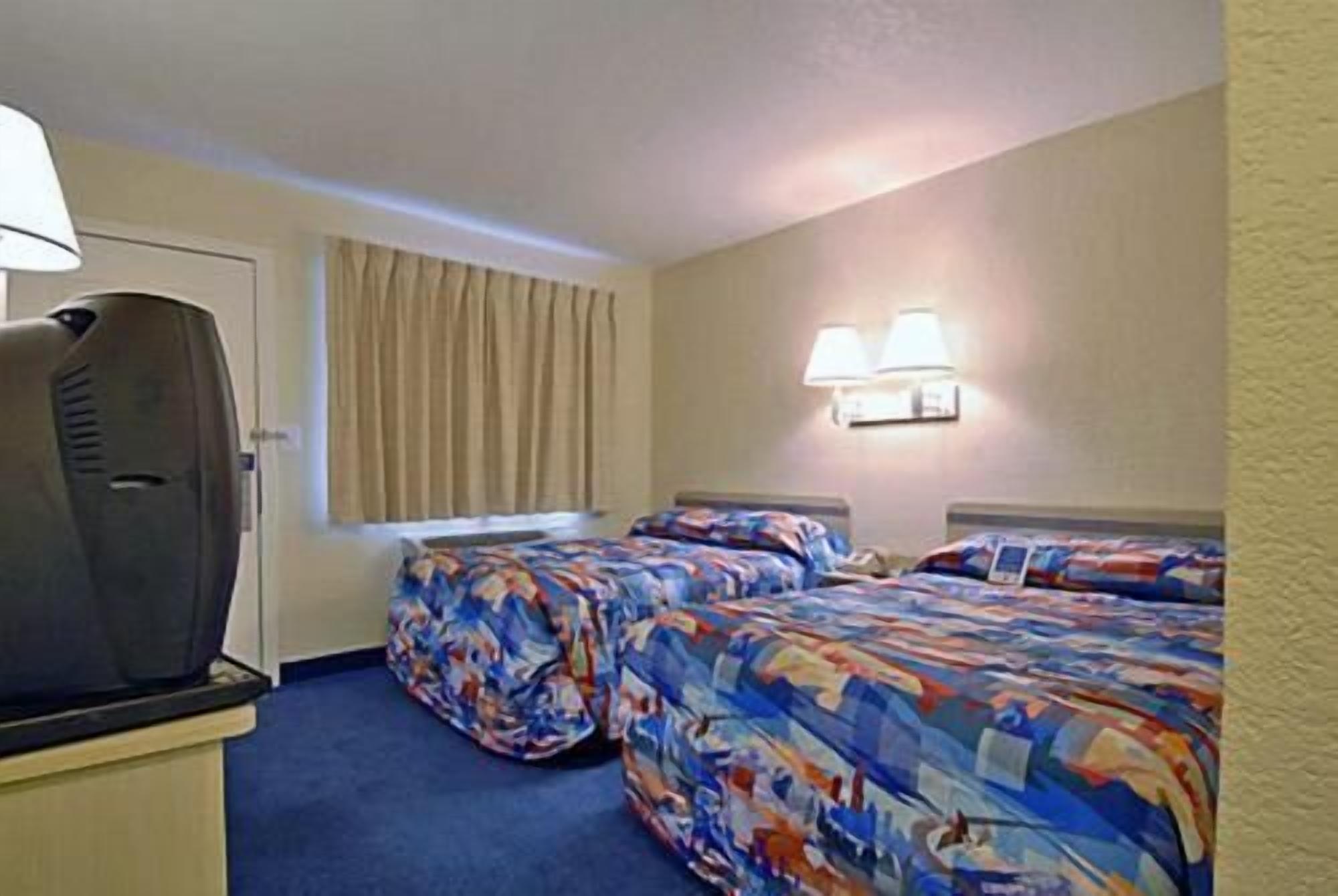 Habitación de hotel con dos camas, televisión y ventana con cortinas.