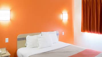 A hotel room with a bed, white bedding, an orange wall, and a telephone on the nightstand.
