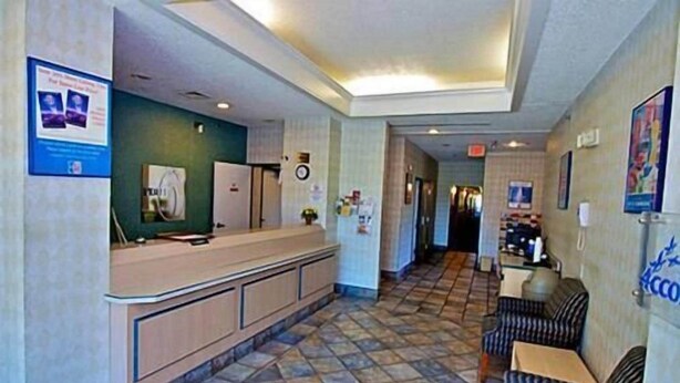 A reception area with a counter, a refrigerator, a clock, and a seating area with patterned chairs. - Motel 6 Seymour, IN - North (Seymour)