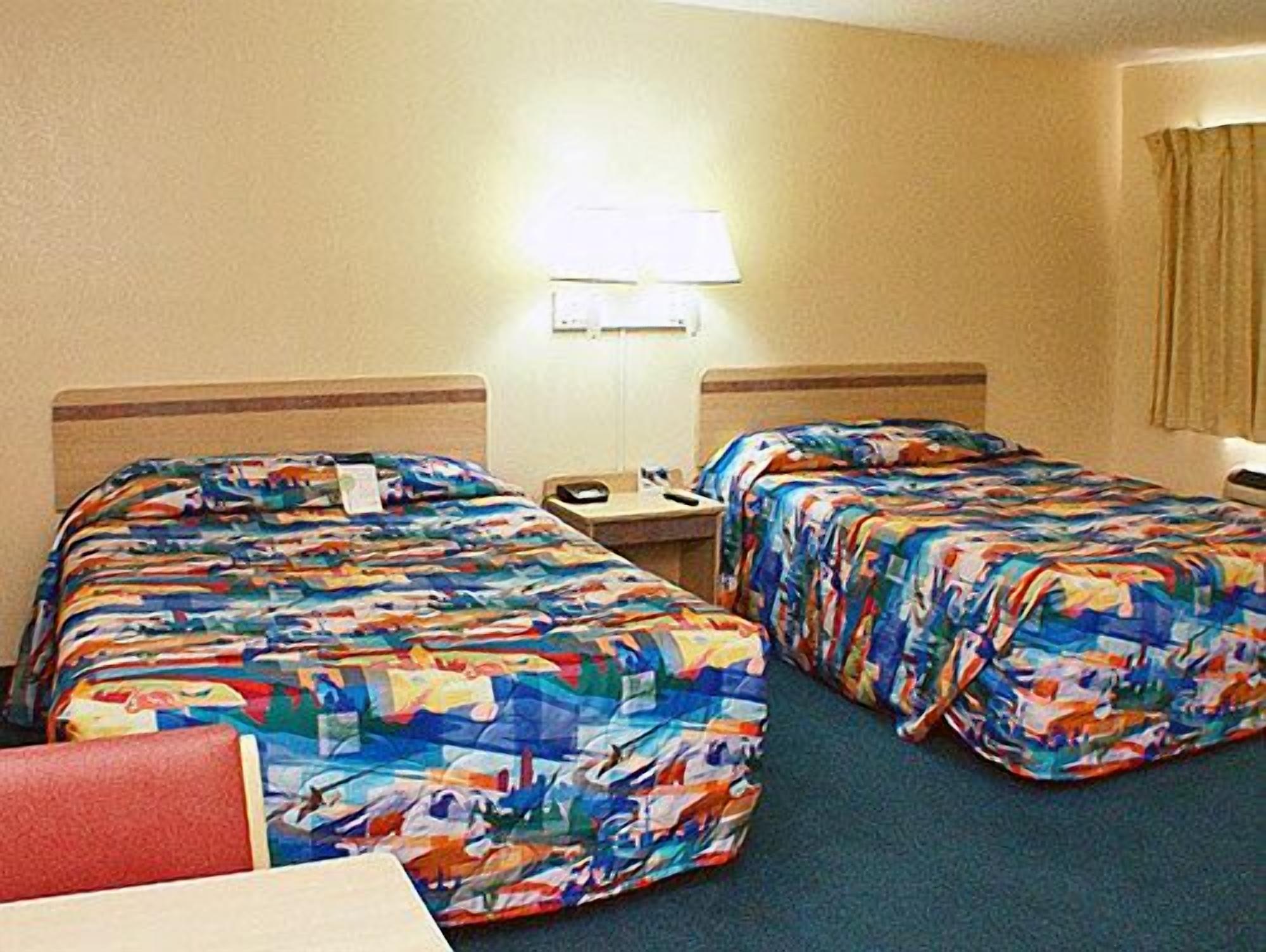 A hotel room with two beds, a nightstand, a lamp, and a red chair.