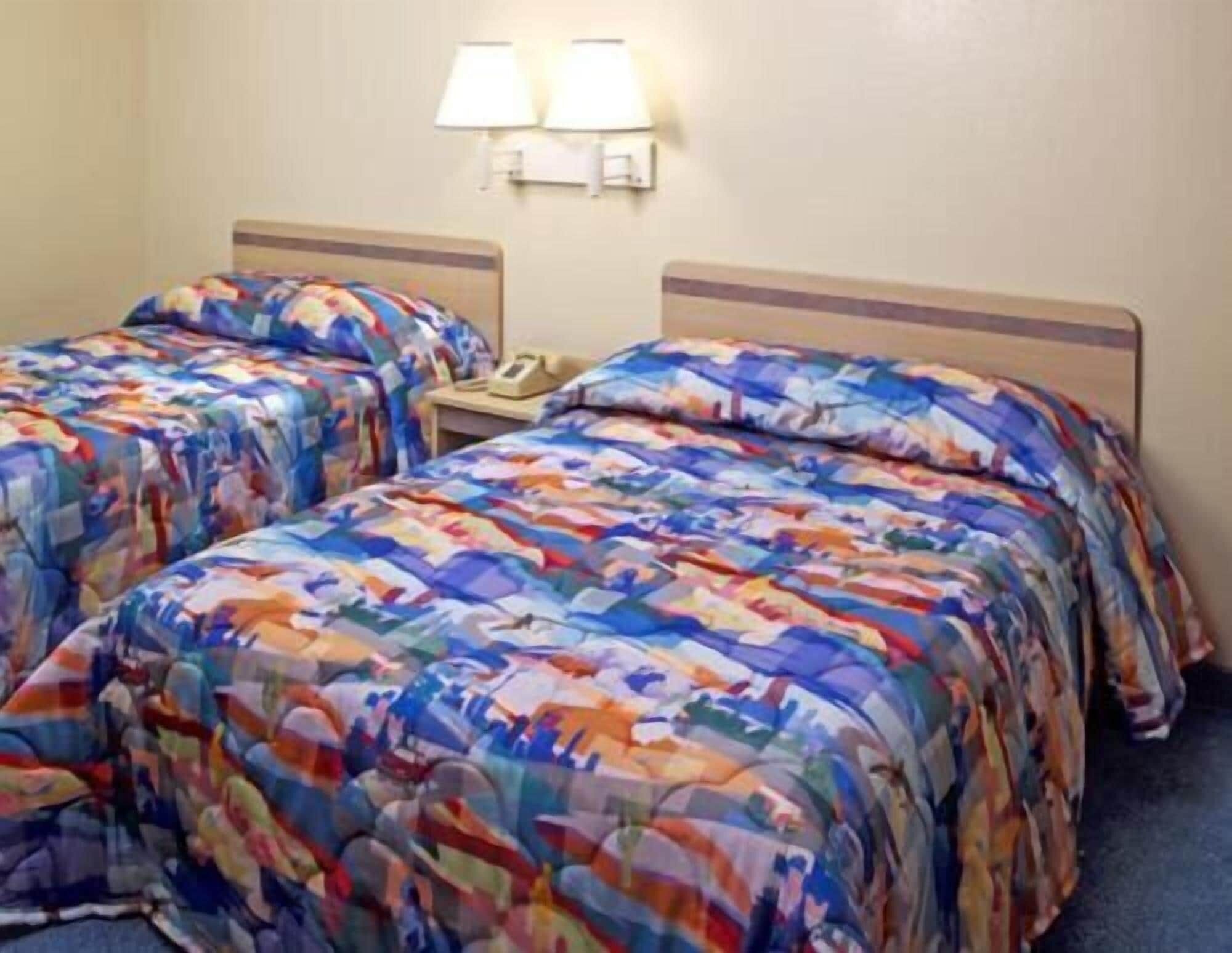 A hotel room with two beds, each with a colorful patterned bedspread. There are two bedside lamps and a telephone on the nightstand.