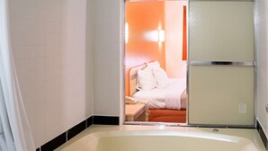 A bathroom with a bathtub, a shower area, and a visible bed with white bedding. - Motel 6 Seymour, IN - North (Seymour)