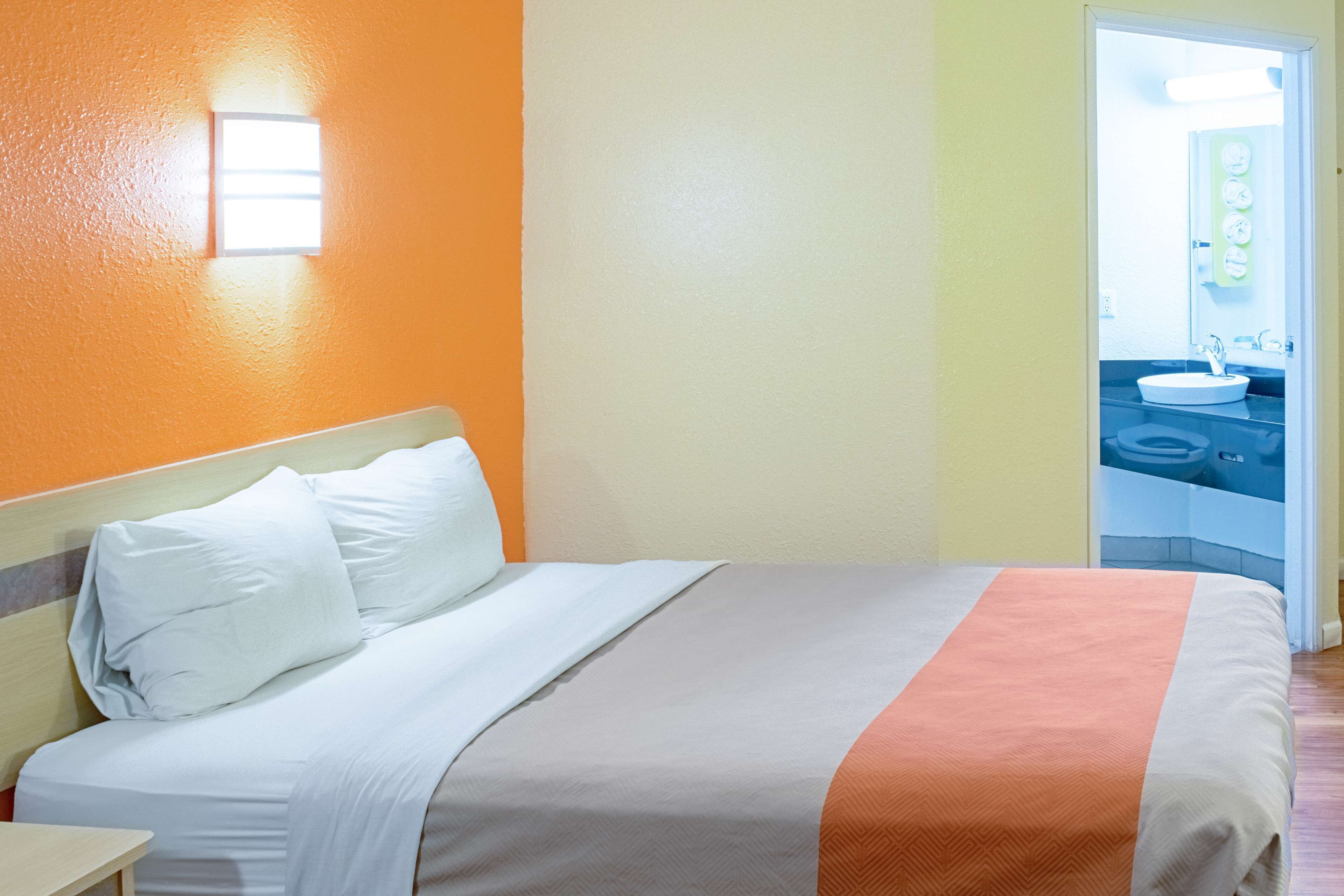 A hotel room with a bed, a nightstand, and a bathroom visible through an open door.
