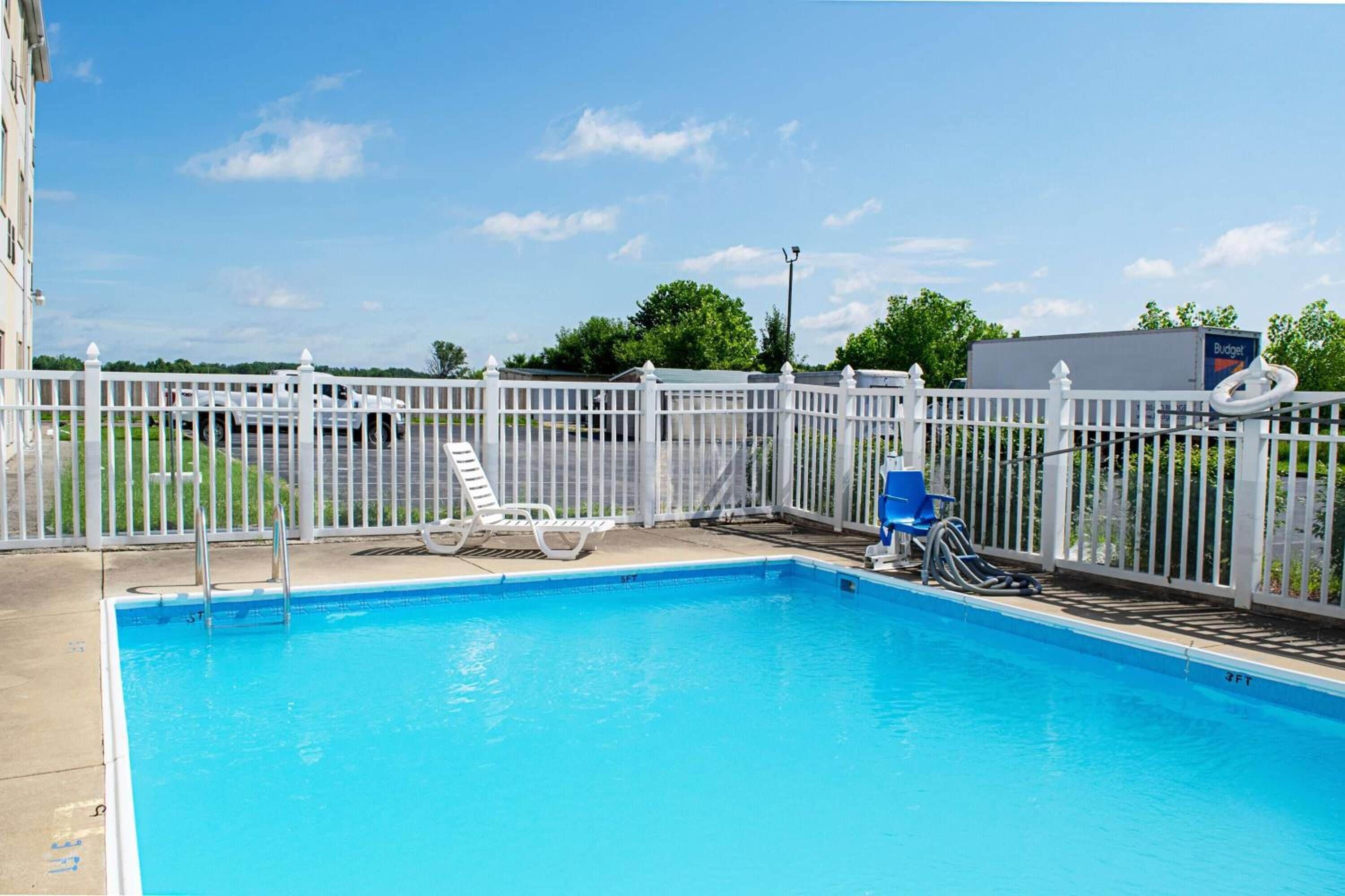 A swimming pool with a white fence, lounge chairs, and a blue chair.