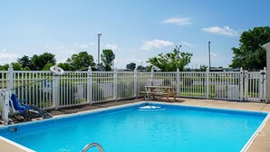 A rectangular swimming pool with a white fence surrounding it, a wooden bench, and a lifeguard chair. - Motel 6 Seymour, IN - North (Seymour)