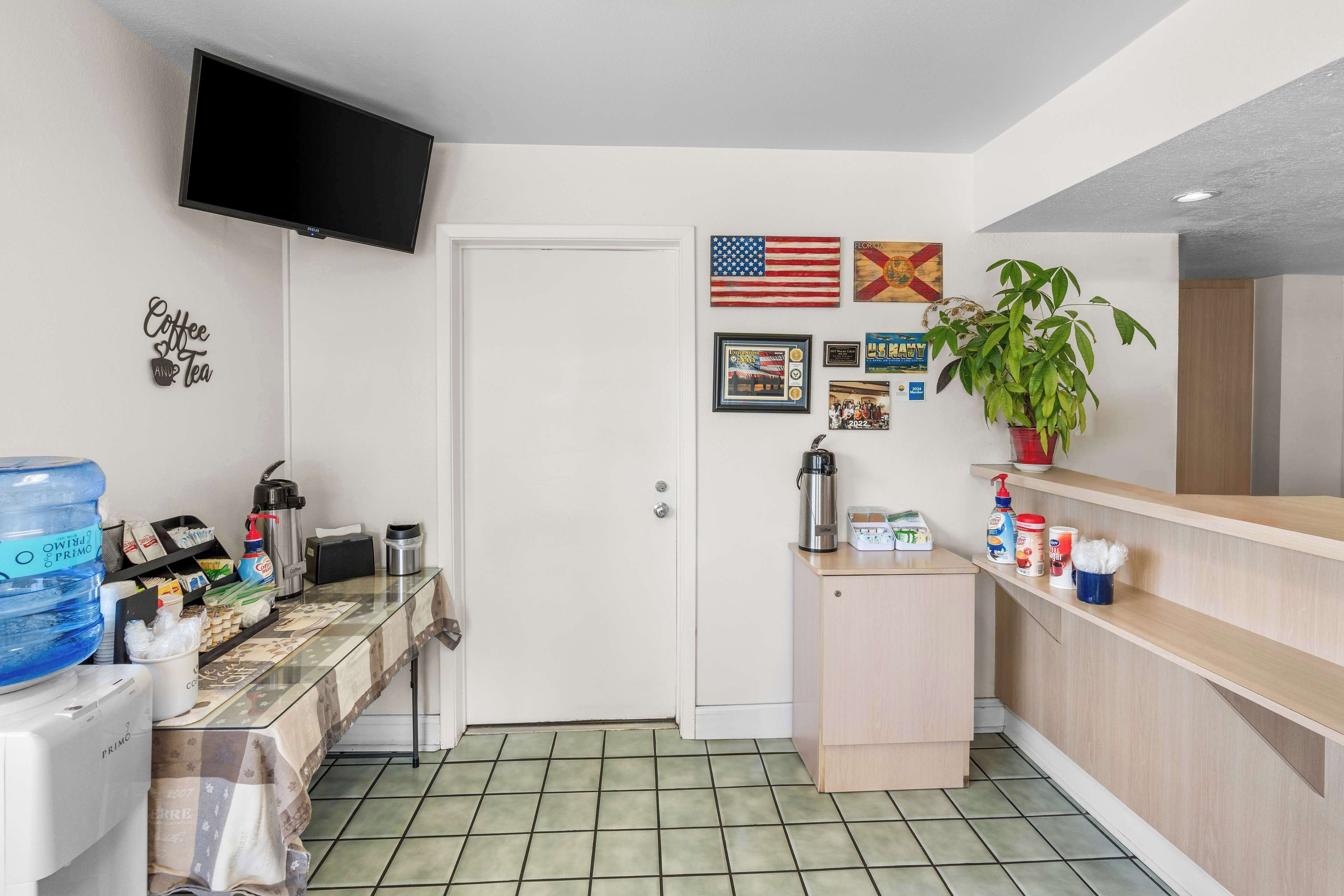 A small kitchenette with a coffee maker, a water dispenser, and a coffee machine. There is a TV mounted on the wall and a plant on the counter.