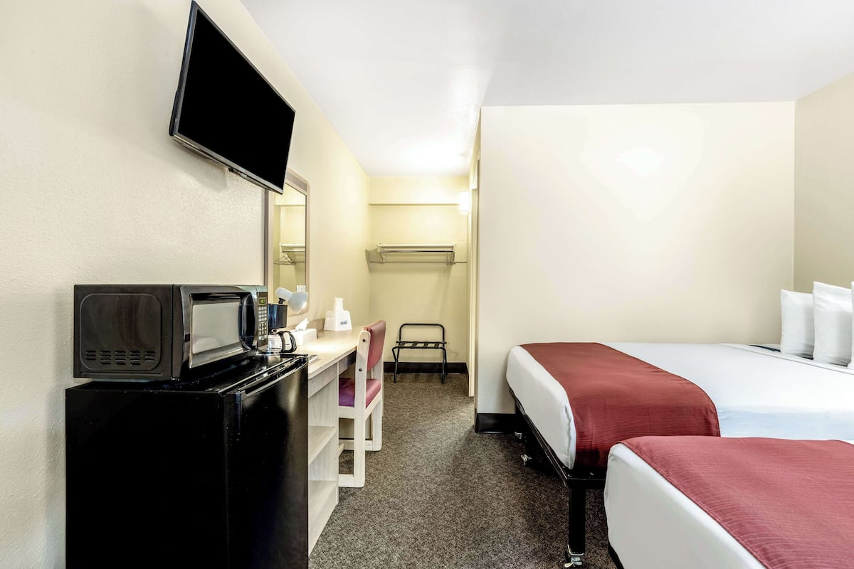 Une chambre d’hôtel comprenant un lit, un bureau avec un micro-ondes, une chaise, un téléviseur fixé au mur et un petit placard.