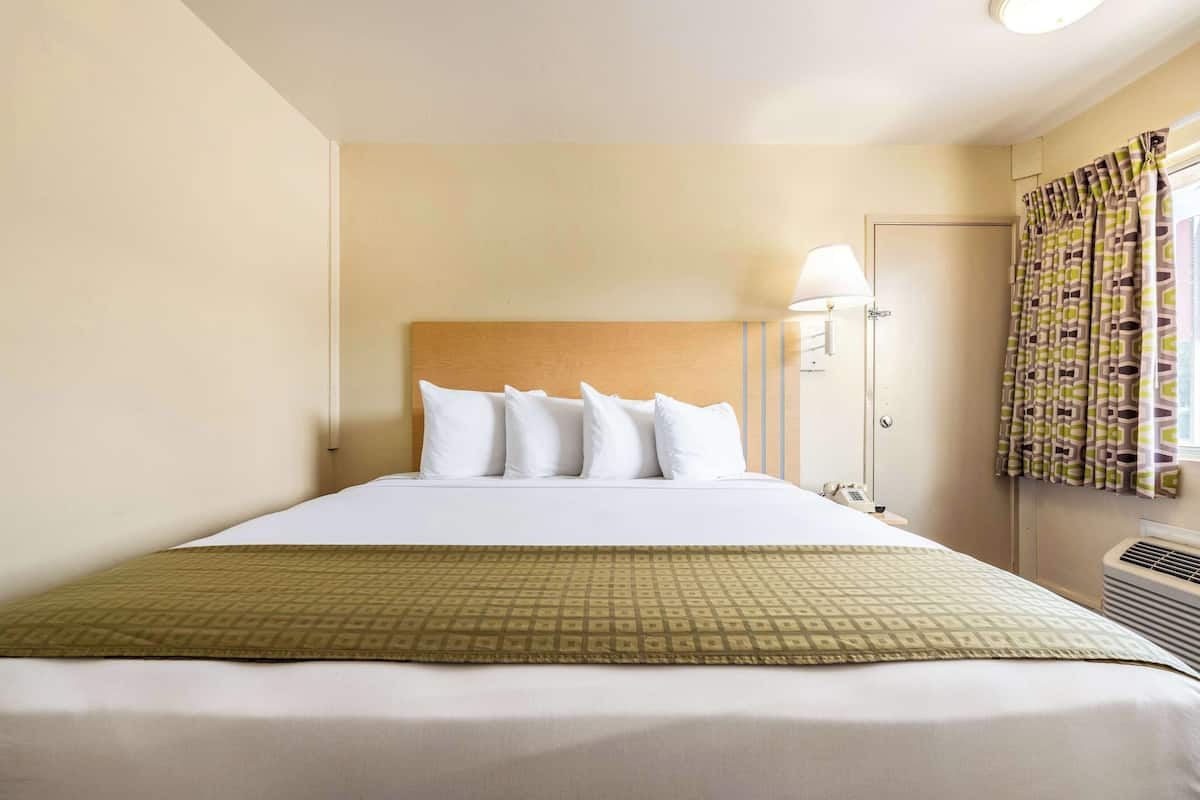 Une chambre d’hôtel comprenant un lit, une lampe de chevet, une fenêtre avec des rideaux et un climatiseur fixé au mur.
