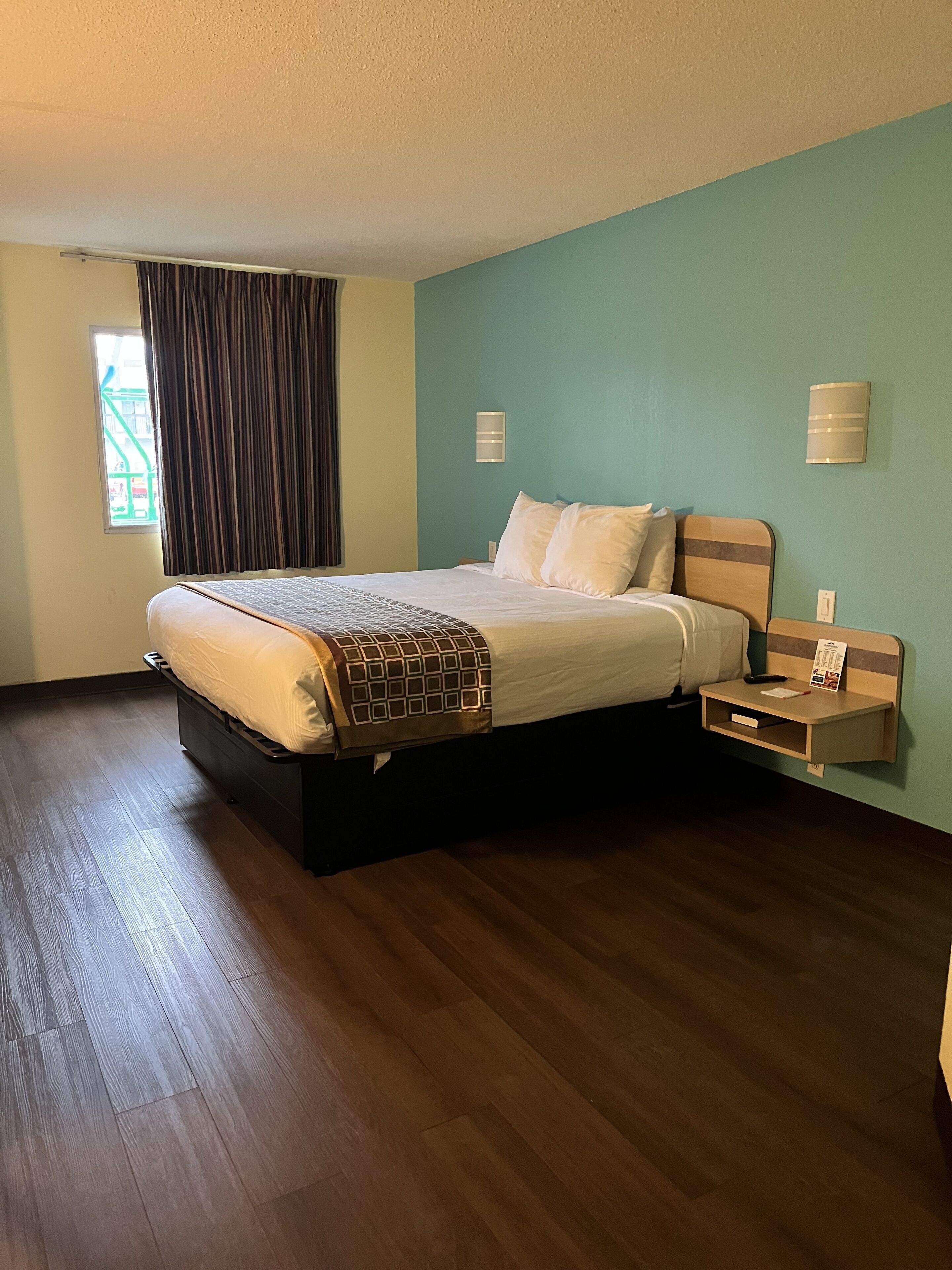 Una camera d'albergo con un letto grande, un comodino e una finestra con tende.