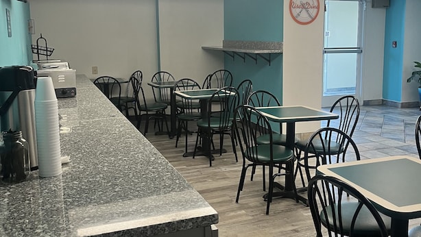 A restaurant interior with a long counter, multiple tables, and chairs. - Howard Johnson by Wyndham Clarksville Tennessee (Clarksville)