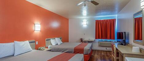 A hotel room with two beds, a desk, a television, and a ceiling fan.