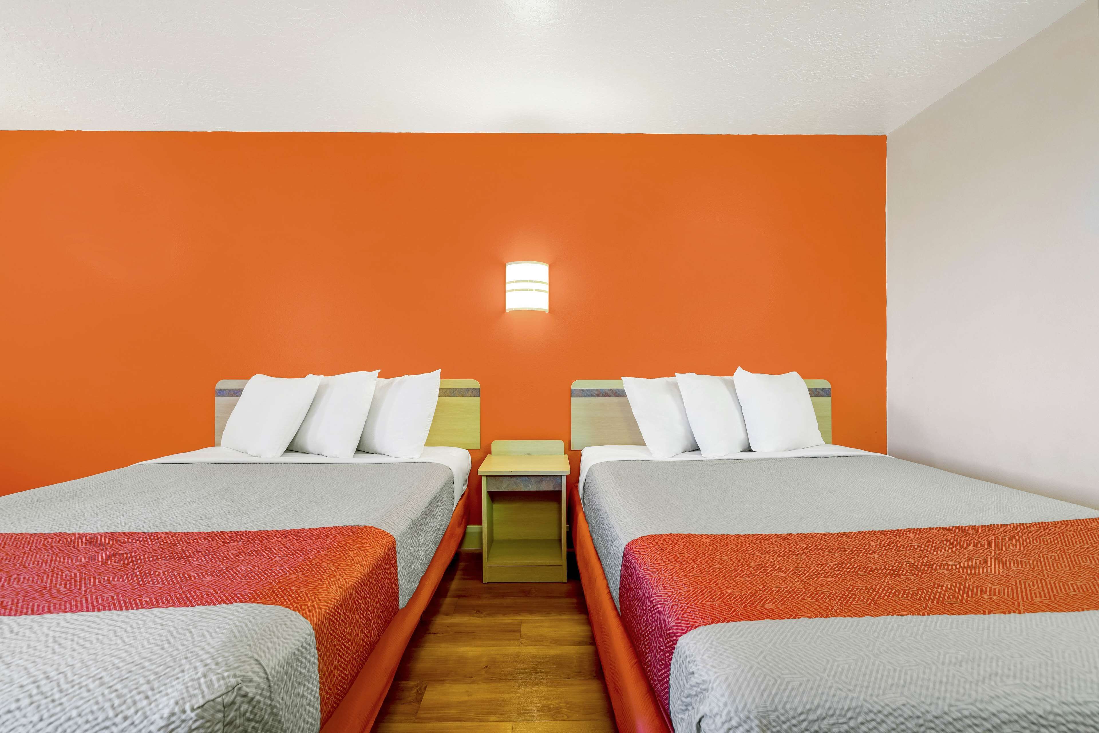 Una camera d'albergo con due letti, pareti arancioni, un comodino e un tavolino.